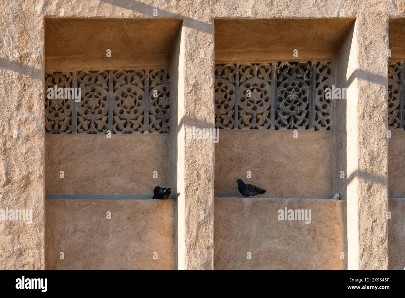 Dubai, VAE - 6. Januar 2024: Tauben sitzen in traditionellen gebogenen Nischen mit komplizierten Gittern im historischen Viertel. Stockfoto