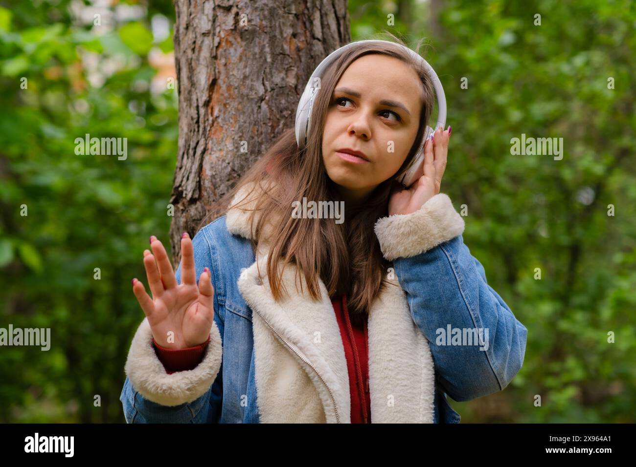 Eine junge Frau lehnt sich an einen Baum, trägt Kopfhörer und genießt Musik im Wald an einem sonnigen Nachmittag Stockfoto
