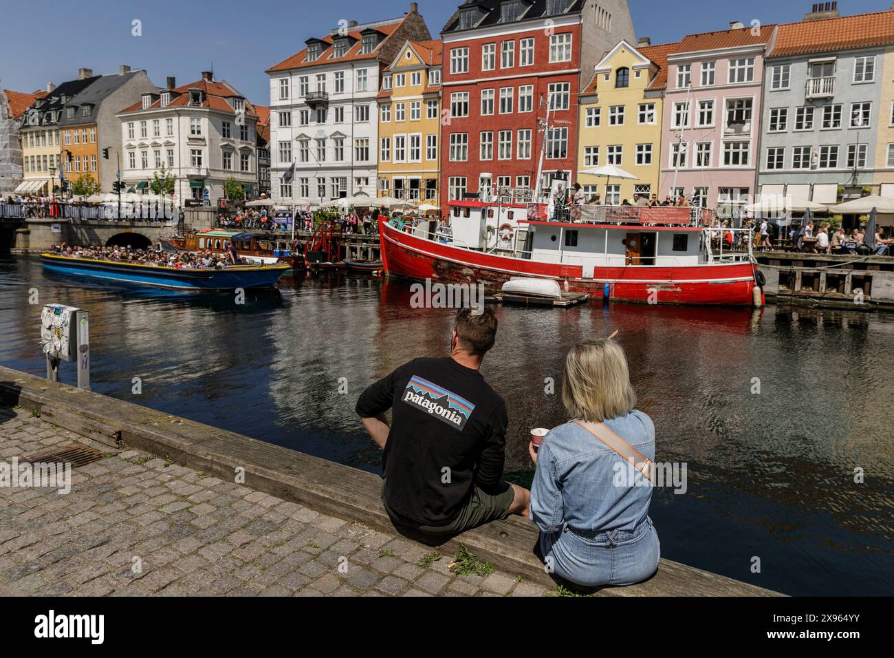 Kopenhagen, Dänemark. Mai 2024. Touristen sitzen auf dem Kanaldamm in der Gegend von Nyhavn ñ, einem beliebten Touristenort, der für seine farbenfrohen historischen Häuser, Bars, Restaurants und Boote bekannt ist. Kopenhagen belegt bei der Mercer Quality of Living Survey 2023 weltweit den vierten Platz. Eine stabile Wirtschaft, ausgezeichnete Bildungsangebote und hohe soziale Sicherheit machen es für Einheimische und Touristen attraktiv. Kopenhagen ist auch eine der teuersten Städte der Welt und ein beliebtes Touristenziel. (Foto: Volha Shukaila/SOPA Images/SIPA USA) Credit: SIPA USA/Alamy Live News Stockfoto