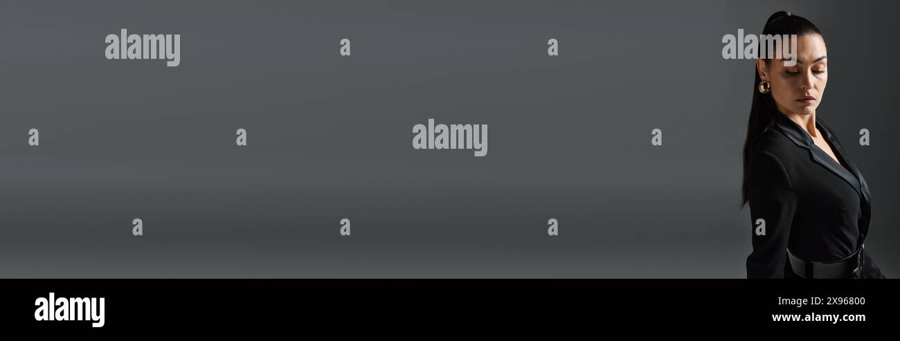 Eine Frau in einem schwarzen Hemd steht vor einem grauen Hintergrund. Stockfoto
