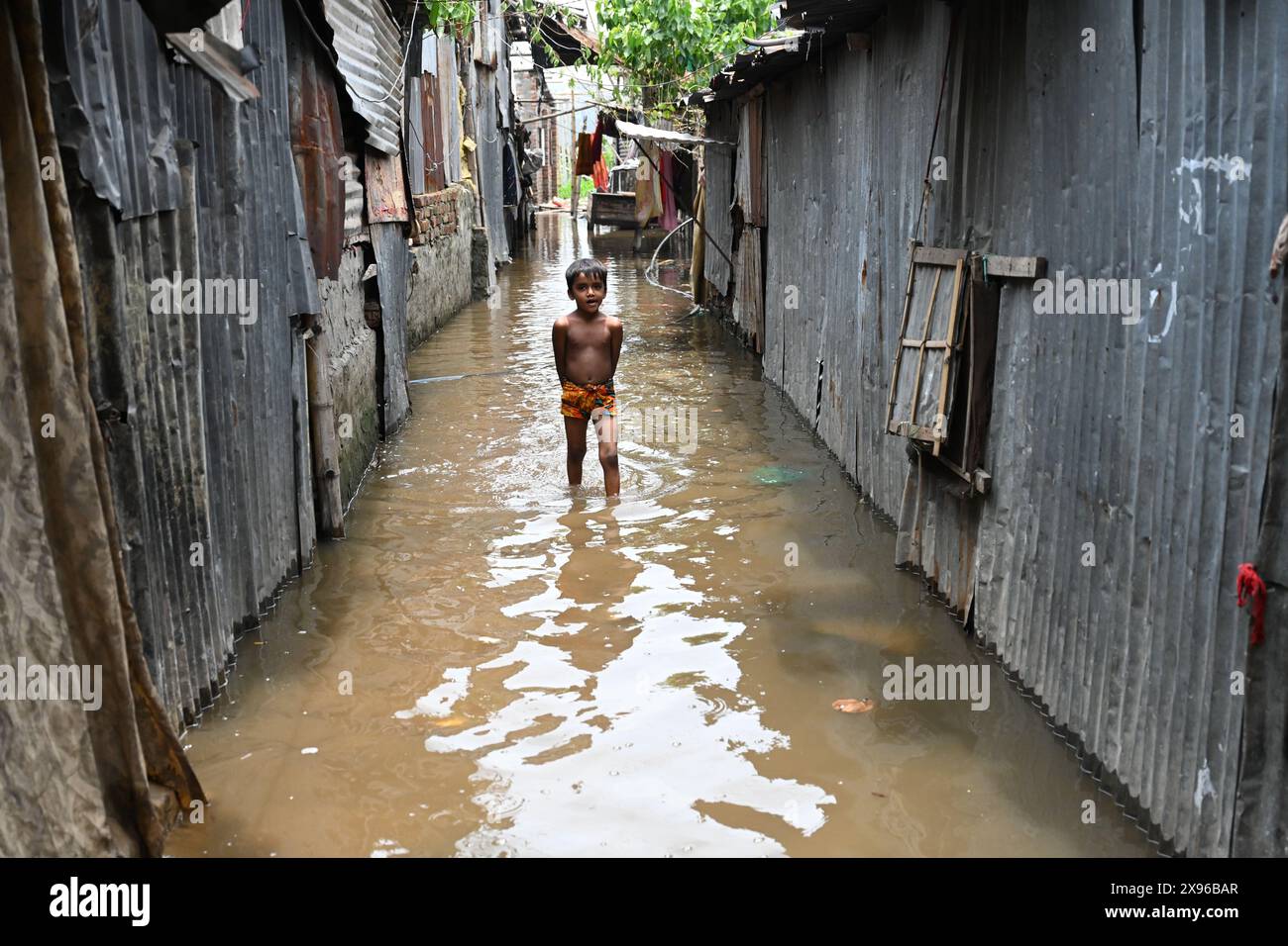 Ein Slumkind waten durch einen überfluteten Innenhof, nachdem der Zyklon Remal am 29. Mai 2024 im Balumath-Slum in Dhaka, Bangladesch, gelandet war Stockfoto