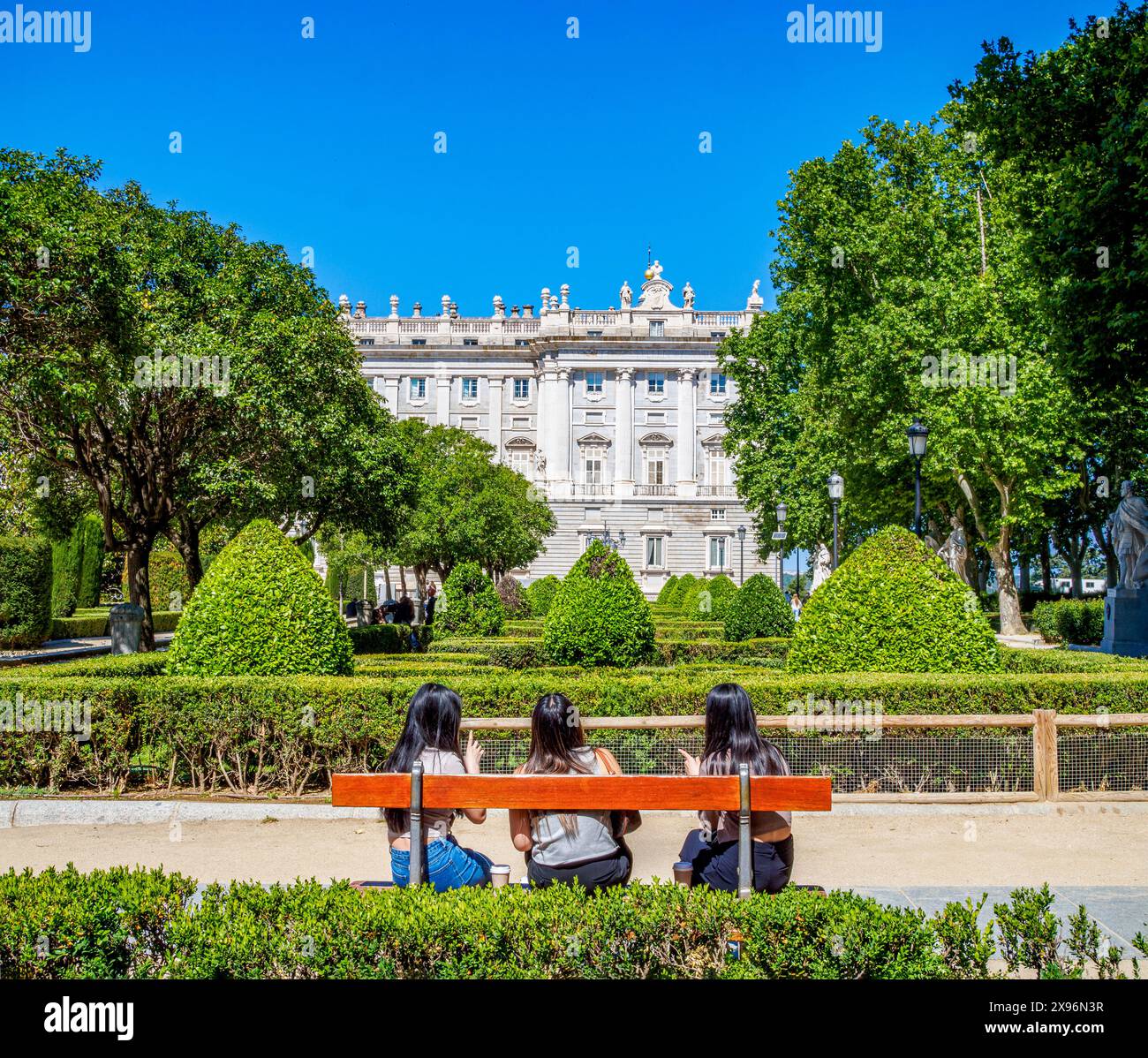 Touristen sitzen an einem sonnigen Tag auf einer Bank mit Blick auf den Königspalast von Madrid. Madrid, Spanien. Stockfoto
