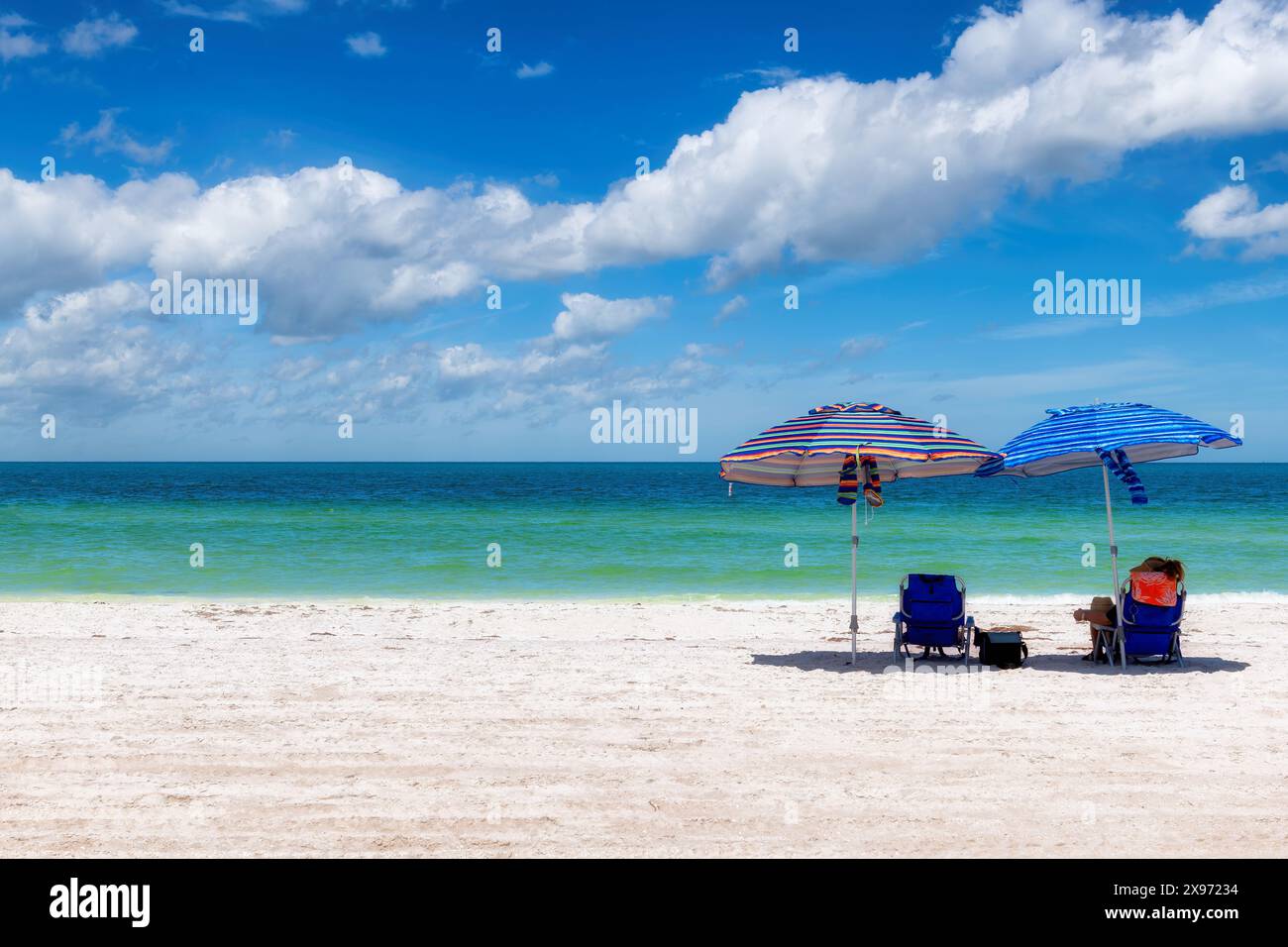 Sonniger Strand mit buntem Sonnenschirm und Liegen am tropischen Strand Stockfoto Sonniger Strand mit buntem Sonnenschirm und Liegen am tropischen Strand Stockfoto