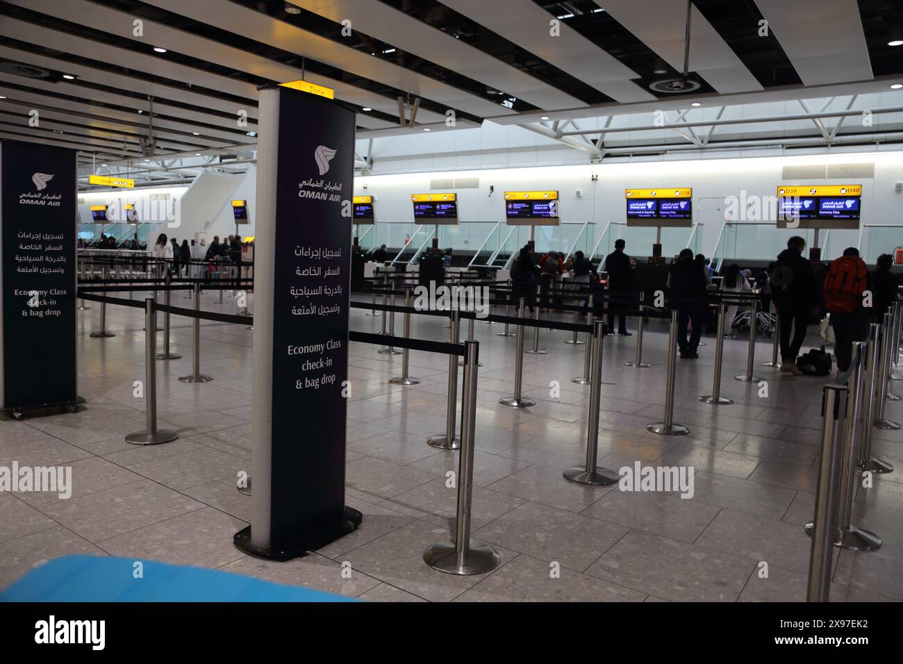 Passagiere am Flughafen London Heathrow stehen beim Check-in in in der Warteschlange und werden mit dem Gepäck für Omani Air England abgesetzt Stockfoto