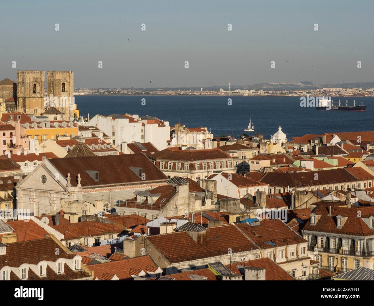 Panorama einer Stadt mit roten Dächern, großen historischen Gebäuden am Wasser und einem Frachtschiff im Hafen, Blick auf die Altstadt von Lissabon auf dem Stockfoto