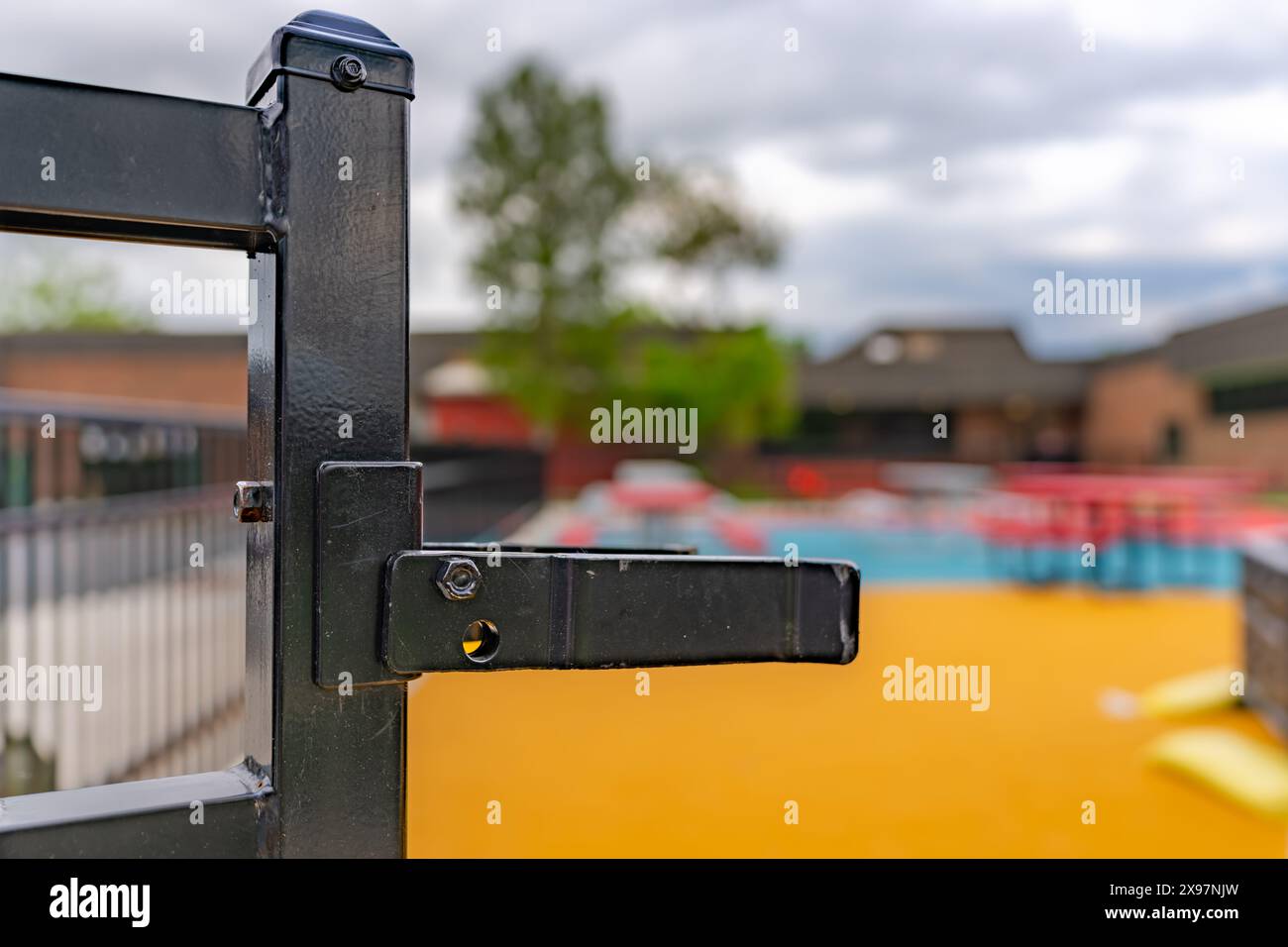 Nahaufnahme eines dekorativen schwarzen Metallzaun-Torriegels auf einem farbenfrohen Spielplatz. Stockfoto