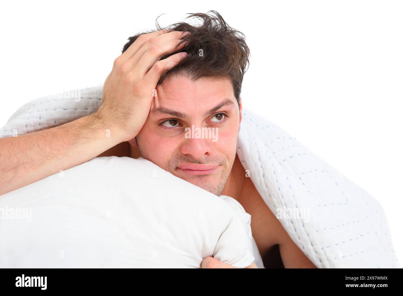 Nahporträt eines frustrierten, verärgerten jungen Mannes, der auf weißem Hintergrund im Bett liegt Stockfoto