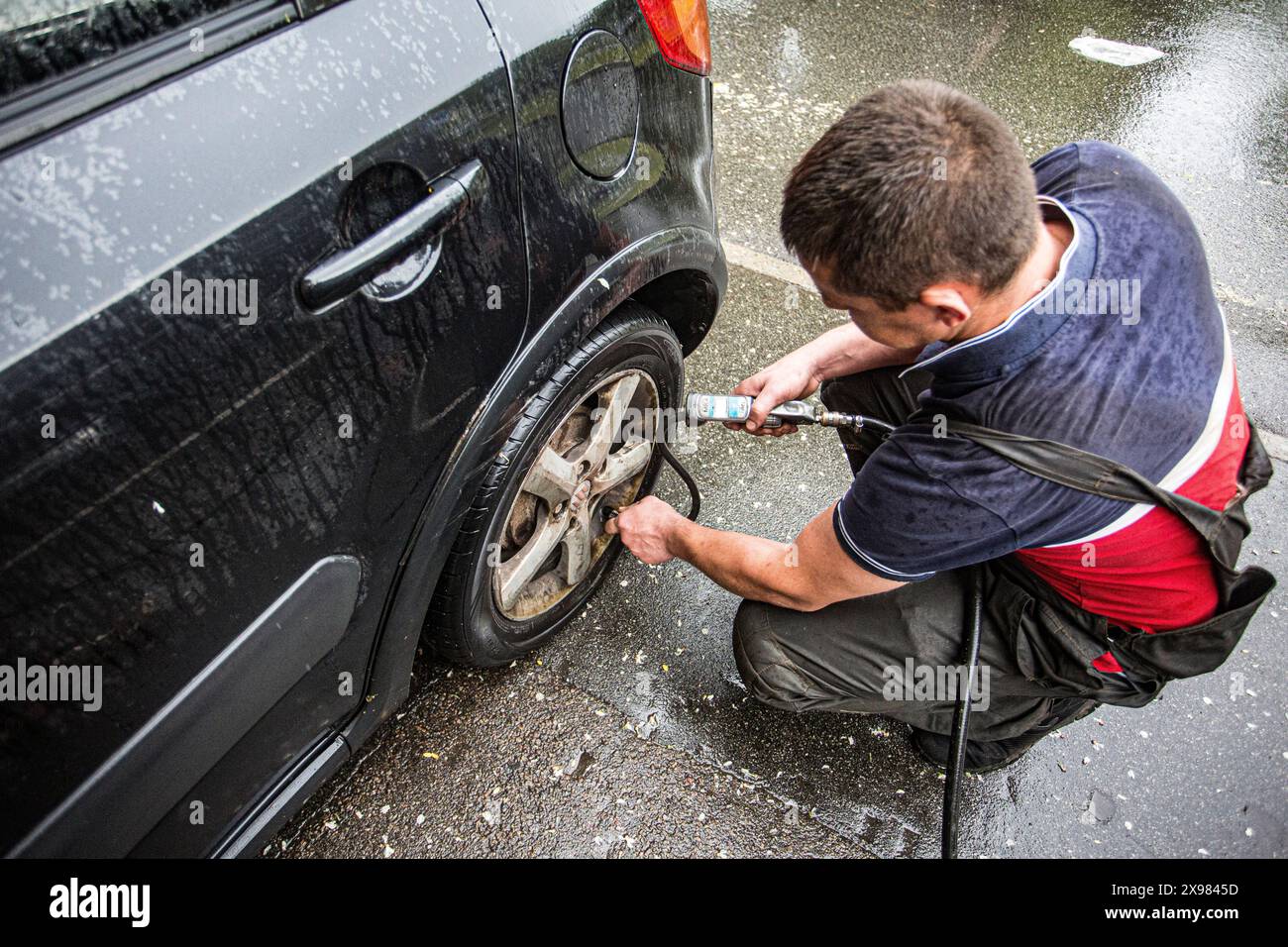 Der Mechaniker in Kiew, Ukraine, überprüft den Reifendruck unter Regen, eine gewöhnliche Sache während der 24-Stunden-Schicht Stockfoto