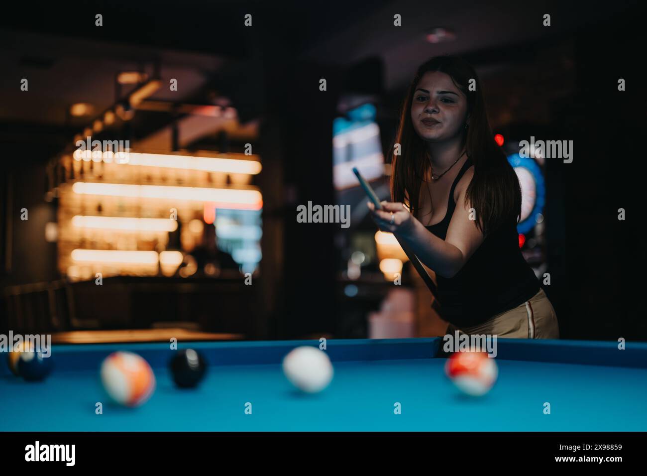 Junge Frau, die in einer Bar mit stilvoller Beleuchtung Billard spielt Stockfoto