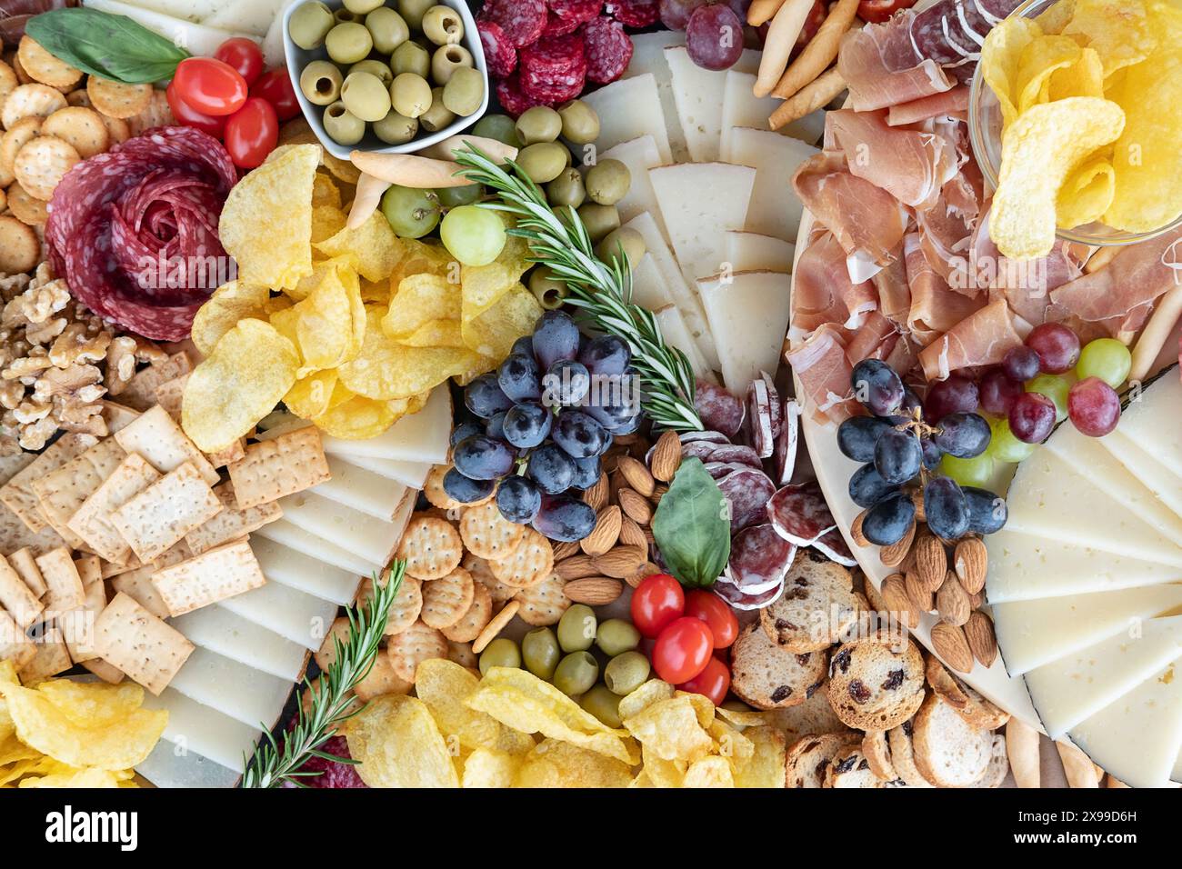 Flaches Wurstbrett, üppig angeordnet mit verschiedenen Aufschnitten, einer Auswahl an gereiften Käsesorten, Crackern und Brotstangen, Nüssen und Oliven Stockfoto