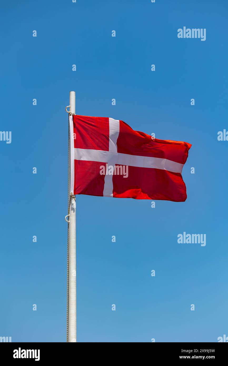 Dänische Flagge am Pfosten, die im Wind weht wolkenlos blauer Himmel Hintergrund Stockfoto