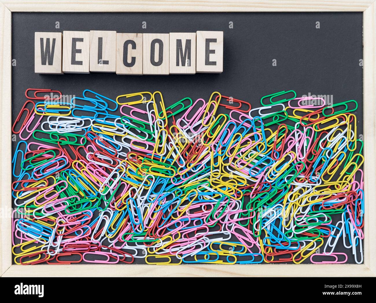 Schwarze Tafel mit bunten Büroklammern und Holzwürfeln mit dem Text: Welcome Stockfoto