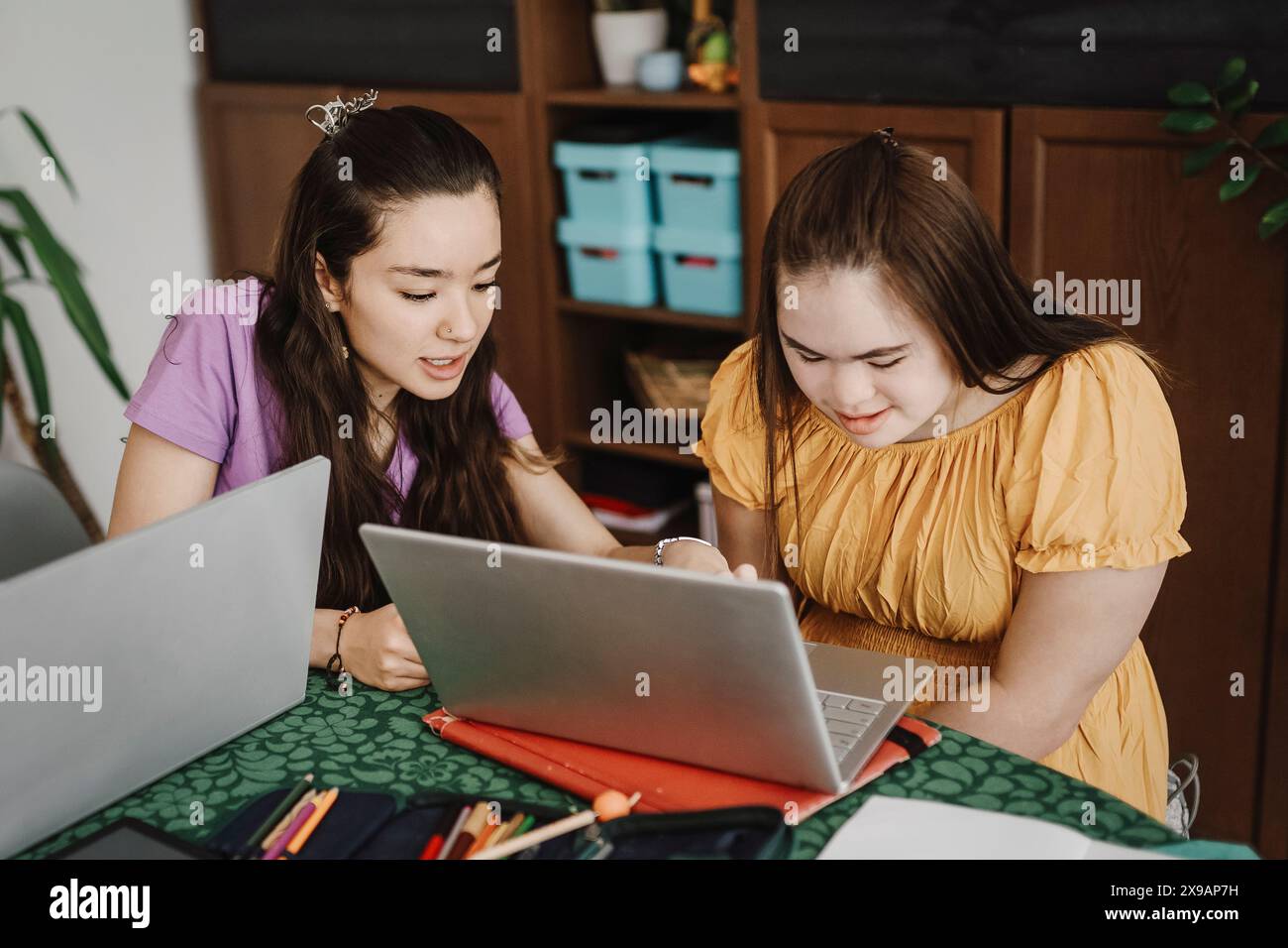 Mädchen, das Schwester mit Down-Syndrom hilft, zu Hause mit Laptop zu lernen Stockfoto