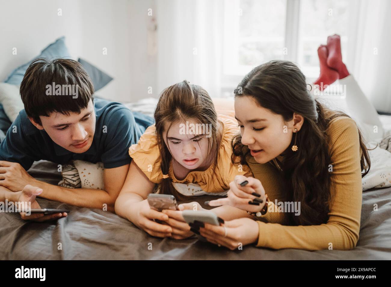 Neugierige männliche und weibliche Geschwister teilen sich ihr Smartphone, während sie zu Hause auf dem Bett liegen Stockfoto