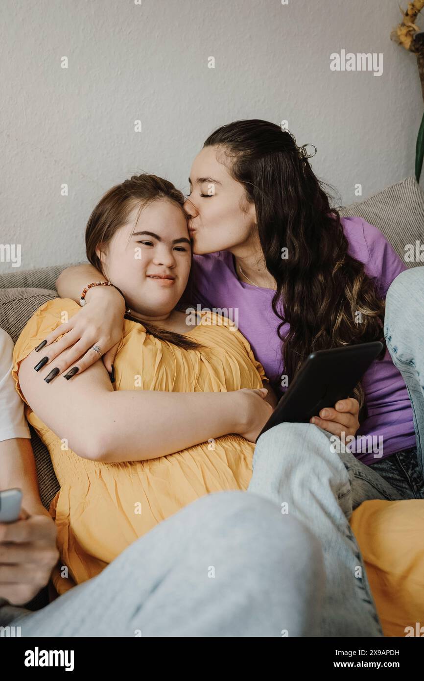 Frau küsst die Schwester des Syndroms, während sie mit einem Teenager-Bruder zu Hause auf dem Sofa sitzt Stockfoto