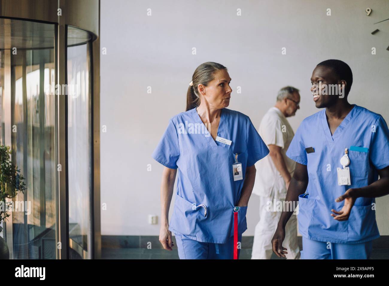 Multirassische Gesundheitspersonal in blauen Scrubs diskutieren beim Gehen im Krankenhaus Stockfoto