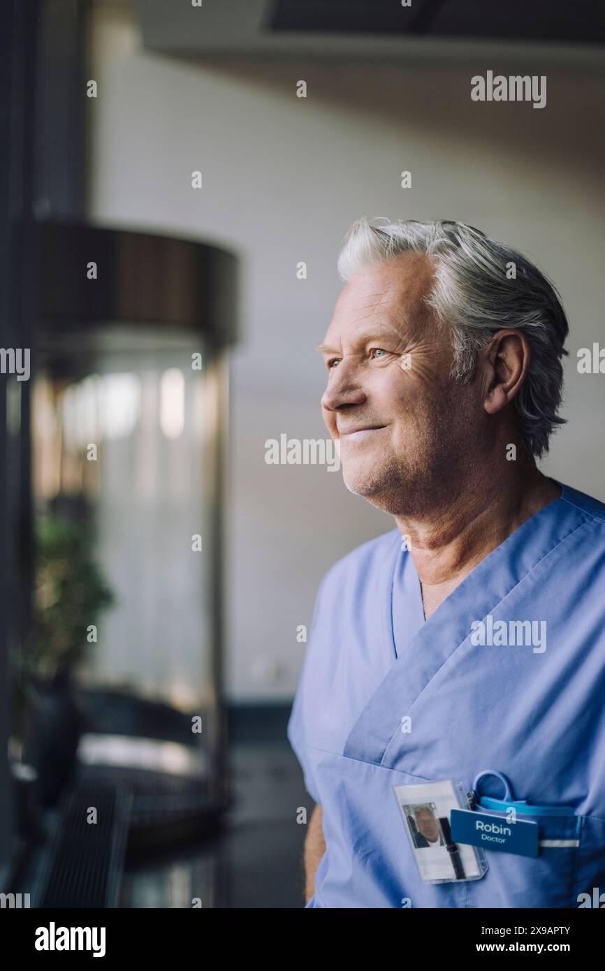 Lächelnder kontemplativer Oberarzt in blauem Peeling im Krankenhaus Stockfoto