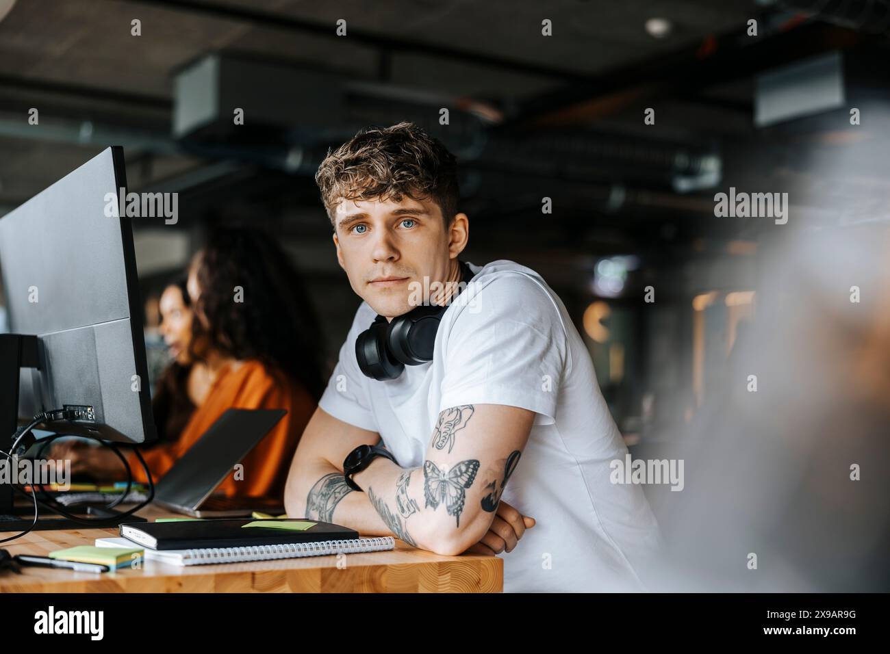 Porträt eines jungen männlichen Unternehmers, der sich am Schreibtisch im Büro auf Ellbogen stützt Stockfoto