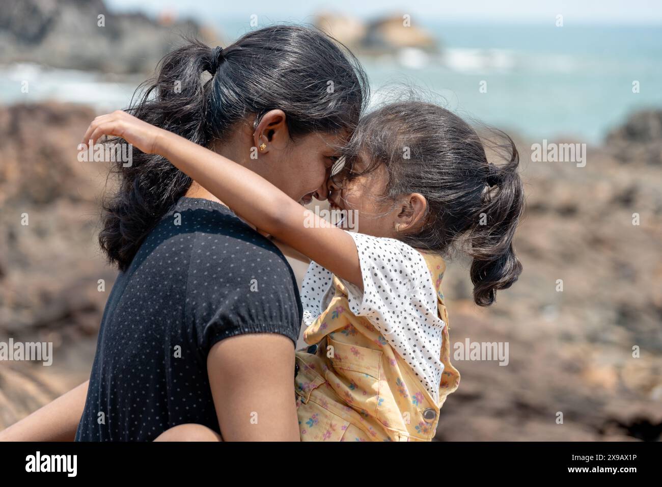 An einer zerklüfteten Küste stehen eine Mutter und ihr kleines Kind nahe und blicken auf das Meer. Ihre Verbundenheit ist offensichtlich, als die Wellen hinter ihnen brechen. Stockfoto