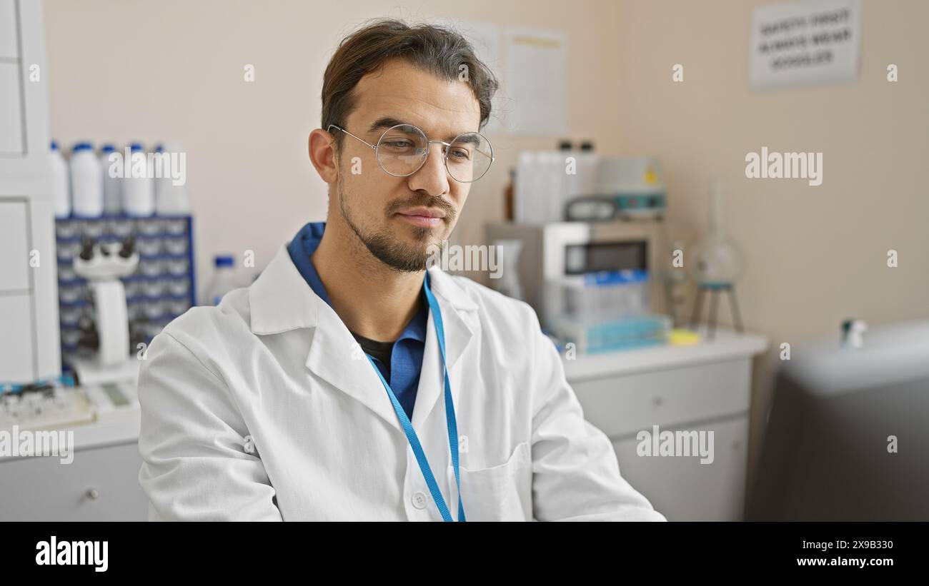 Hübscher junger hispanischer Mann mit Bart, Brille und Labormantel in einem wissenschaftlichen Labor Stockfoto