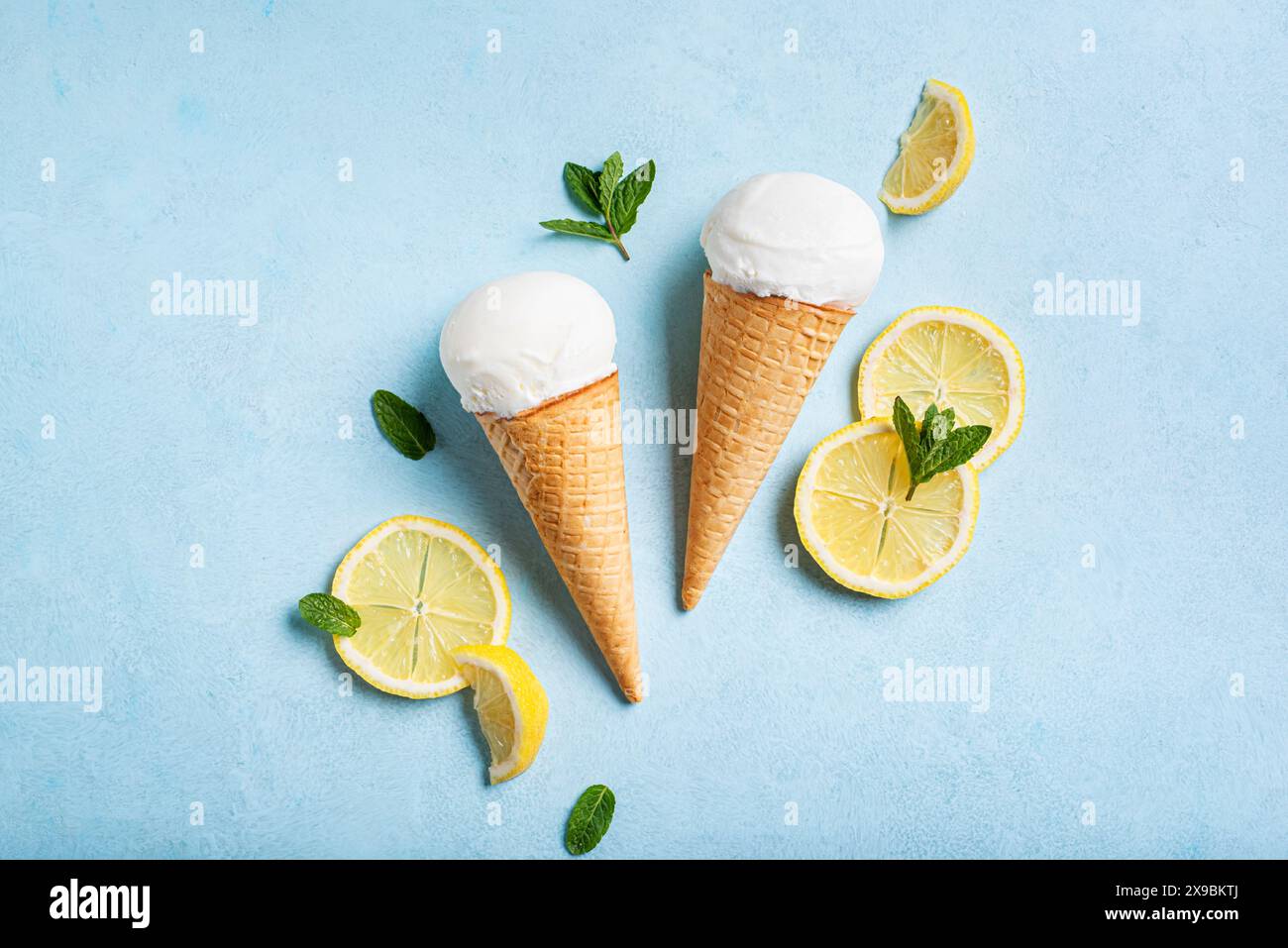 Schaufel Zitroneneis in Waffelkegel und Zitronenscheiben auf hellblauem Hintergrund, Draufsicht. Trendiges, kreatives Layout. Stockfoto