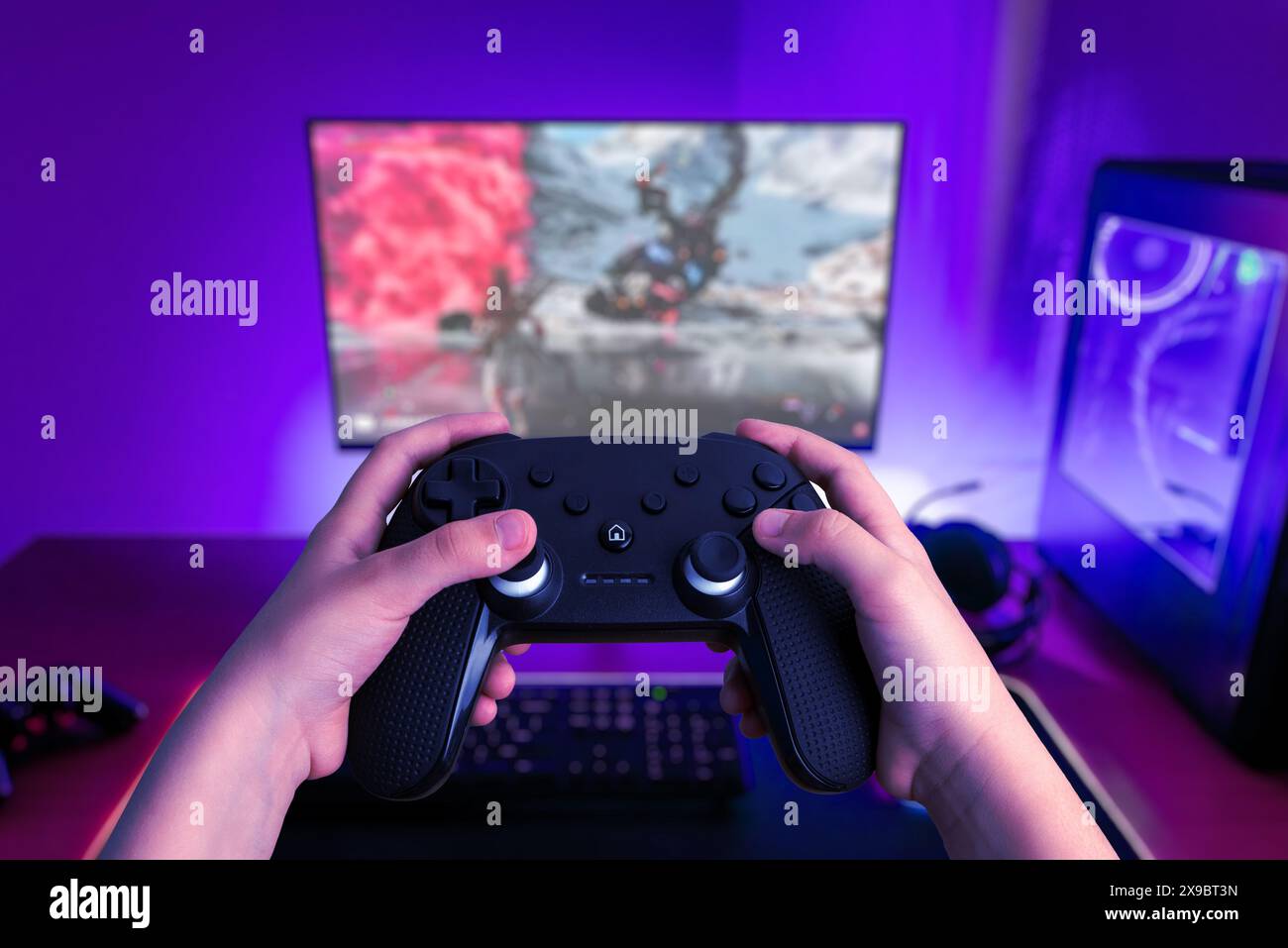 Gamer hält ein Spielpad vor einem glühenden Gaming-PC. Spiele, Technologie und eSports-Inhalte Stockfoto
