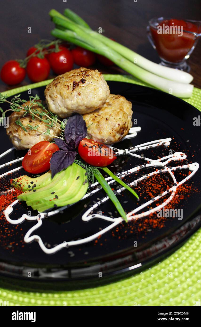 Elegante Präsentation gegrillter Fleischpasteten mit frischem Gemüse und Kräutern auf einem schwarzen Teller Stockfoto