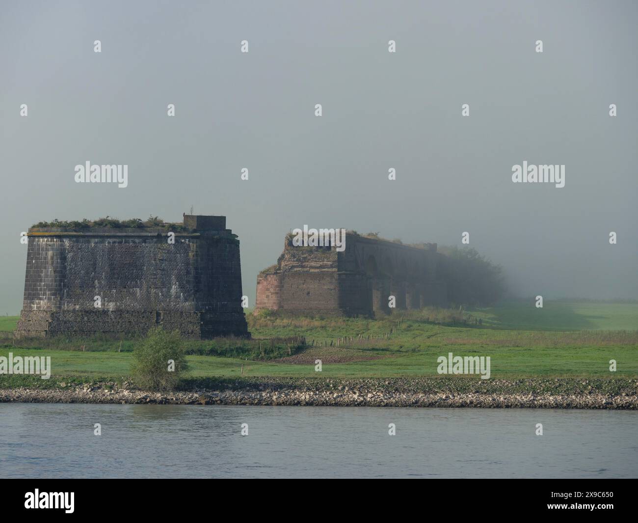 Eine teilweise baufällige Ruine in grüner Landschaft, umhüllt von Nebel, Nebel am rhein mit einer alten Brücke und Schiffen, wesel, Deutschland Stockfoto