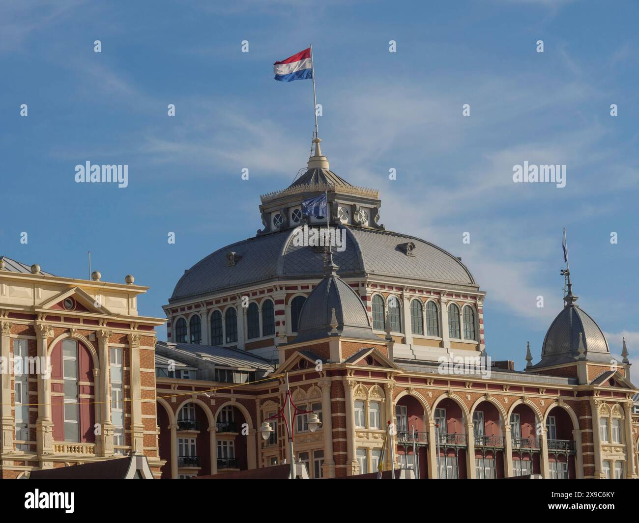 Historisches Gebäude mit niederländischer Flagge vor einem blauen Himmel, der Strand von scheveningen mit Pier und die Promenade, scheveningen, niederlande Stockfoto