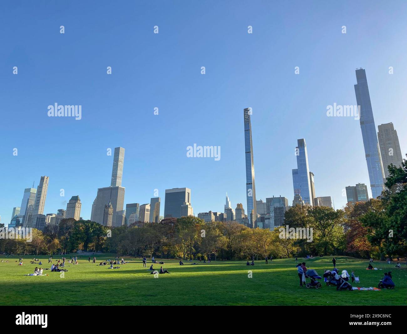 Ein sonniger Tag mit Menschen auf dem Gras im Central Park, umgeben von hohen Wolkenkratzern, die Skyline von New york mit beeindruckenden Wolkenkratzern auf dem Stockfoto