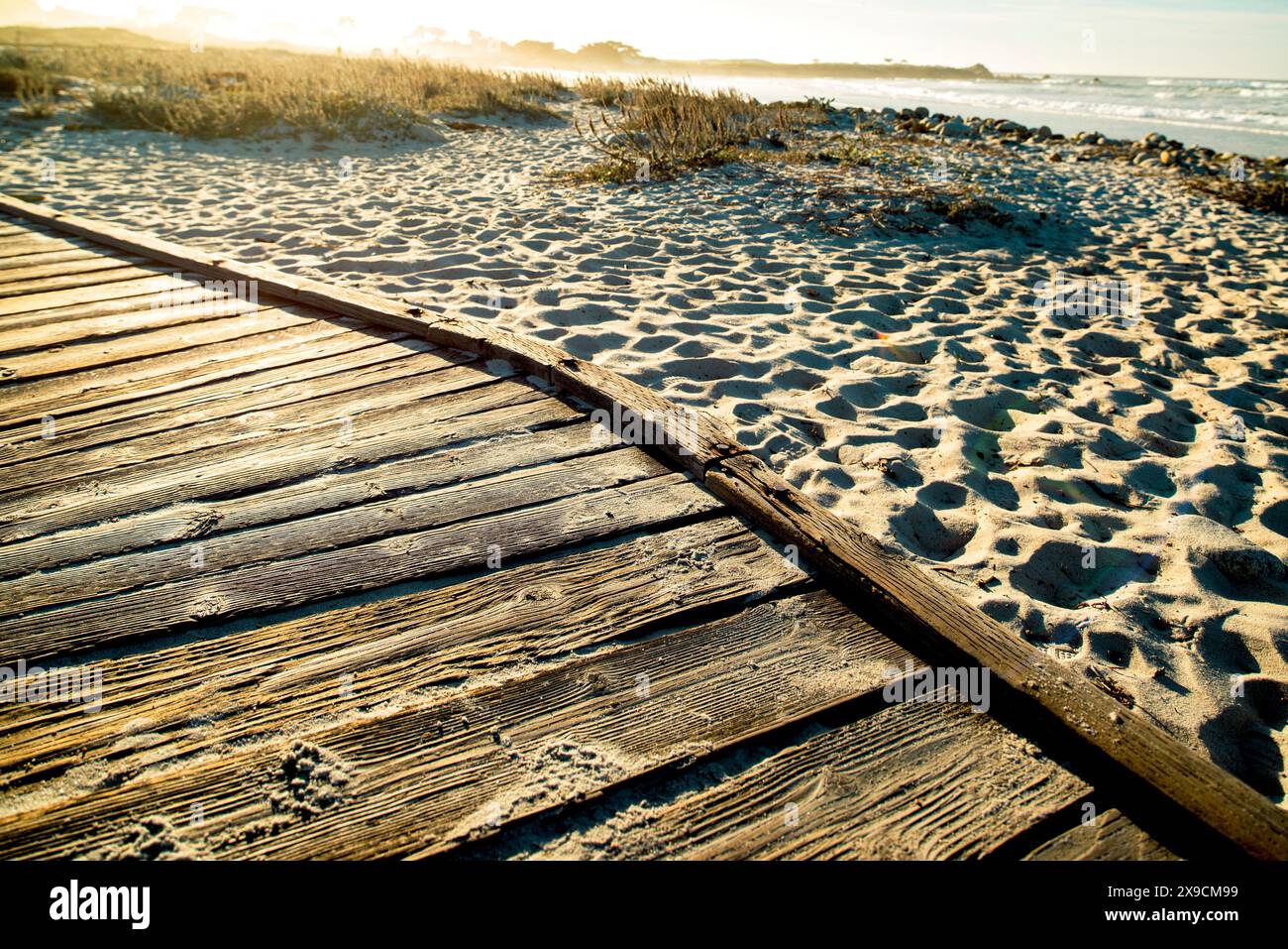 Holzweg an einem kalifornischen Strand in der Nähe der Route 1 bei Sonnenuntergang, mit Sand und Meer im Hintergrund, die eine warme und ruhige Atmosphäre einfangen. Stockfoto