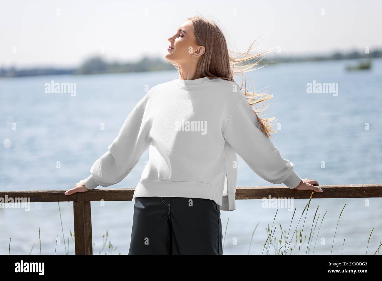 Mockup eines weißen Sweatshirts auf einem blonden Mädchen auf dem Hintergrund des Flusses, Kai, modische Kleidung, Vorderansicht. Frauen-Faultier. Blank elegant A Stockfoto