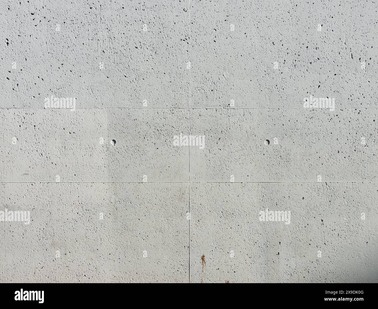 Betonhintergrundstruktur. Rohmaterial einer Gebäudewand mit Poren und Flecken. Echte leere Kulisse, fotografiert von einer Hausfassade. Stockfoto