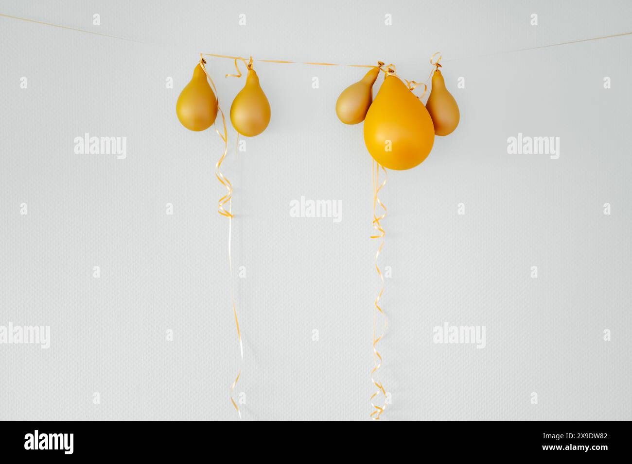 Gelbe Ballons auf weißem Hintergrund mit goldenem String. After-Party-Urlaubskonzept Stockfoto