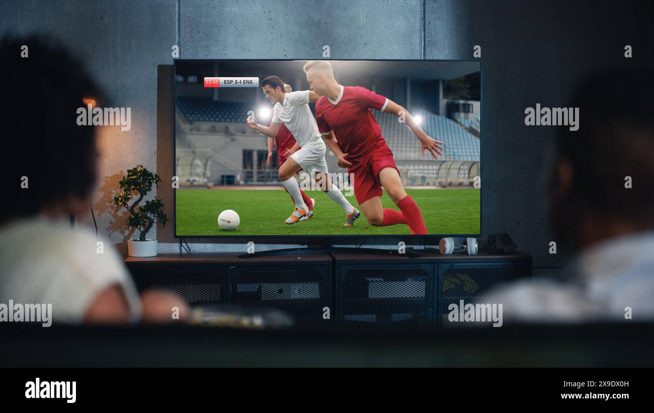 Black Couple Uhren professionelles Fußballspiel im Fernsehen, am Abend auf einer Couch zu Hause. Freund und Freundin Fußballfans sehen sich Sport an. Rückansicht unscharf Nahaufnahme bei Nacht. Stockfoto