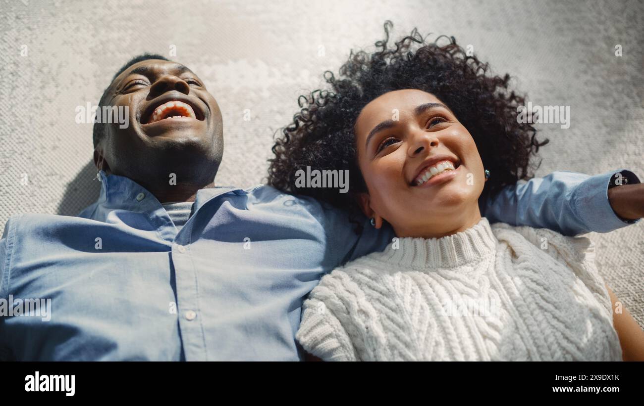 Über dem Porträt eines multiethnischen Paares, das sich auf den Teppich legt und redet, träumt und sich vorstellt. Ehegatten, die einander Fürsorge und Liebe zum Ausdruck bringen. „Zeit Gemeinsam Genießen“-Konzept. Stockfoto