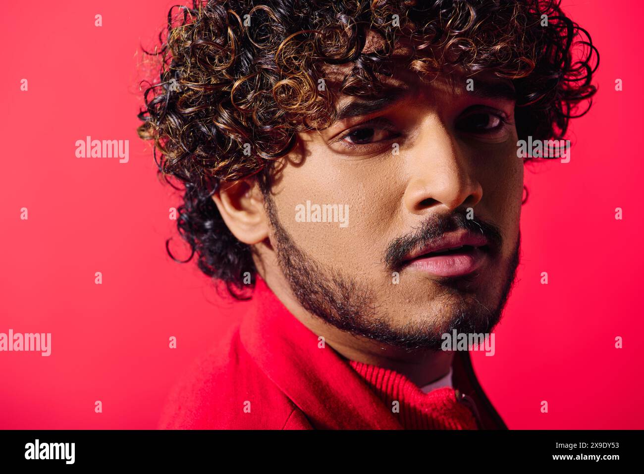 Eine Nahaufnahme eines hübschen jungen Indianers mit lockigen Haaren und intensivem Blick, der sich vor einem lebhaften Hintergrund posiert. Stockfoto