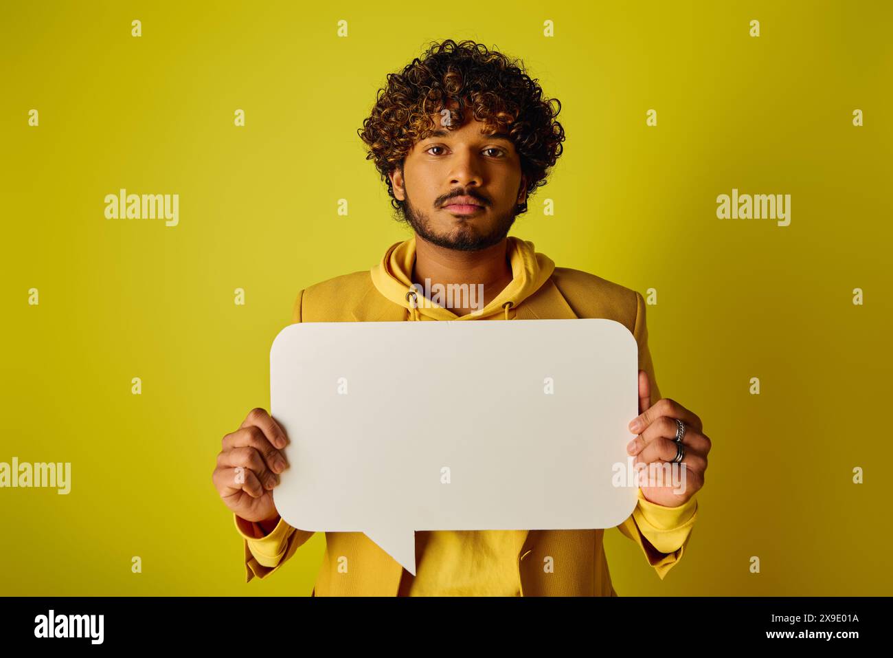 Ein junger Indianer in einem gelben Hoodie, der eine Sprechblase vor einem lebendigen Hintergrund hält. Stockfoto