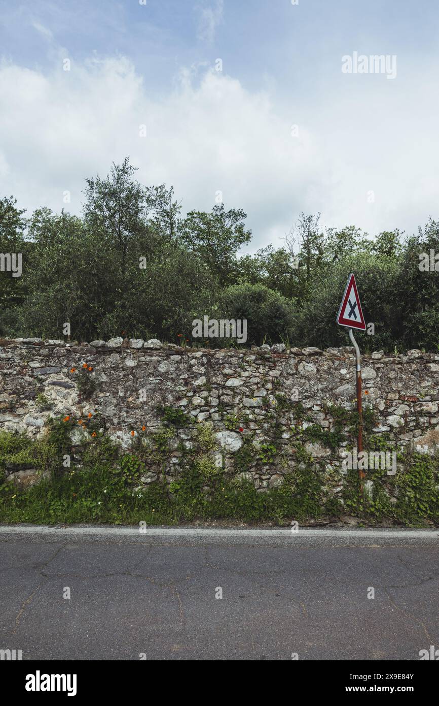 Ein Straßenschild auf einer ruhigen Straße in der ländlichen Toskana in Italien an einem bewölkten Tag mit grauem Himmel, alter Steinmauer und schönen grünen Bäumen im Hintergrund. Stockfoto