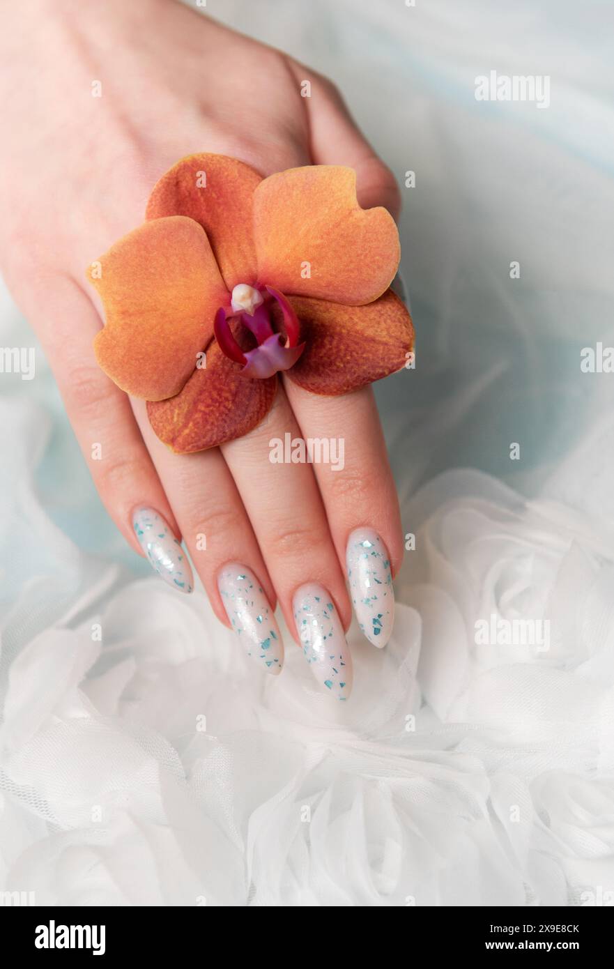 Eine Nahaufnahme zeigt eine Person Hand mit komplizierten, floralen Nailarten, die zart eine Orangenblüte umhüllt. Die umliegende weiche, schwungvolle Textur Stockfoto
