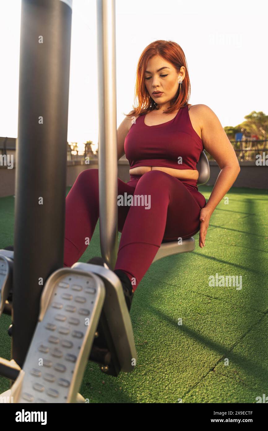 Plus-Size-Frau mit einem Trainingsgerät in einem Outdoor-Gym während Sonnenuntergang - Bestimmung und Fitness Motivation, gesunde Lebensweise, hell und sonnig d Stockfoto