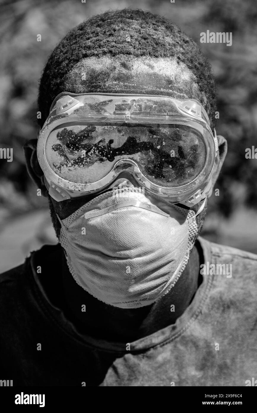 Ein Bauarbeiter bedeckt mit weißem Schleifstaub mit Maske und Schutzbrille. Stockfoto