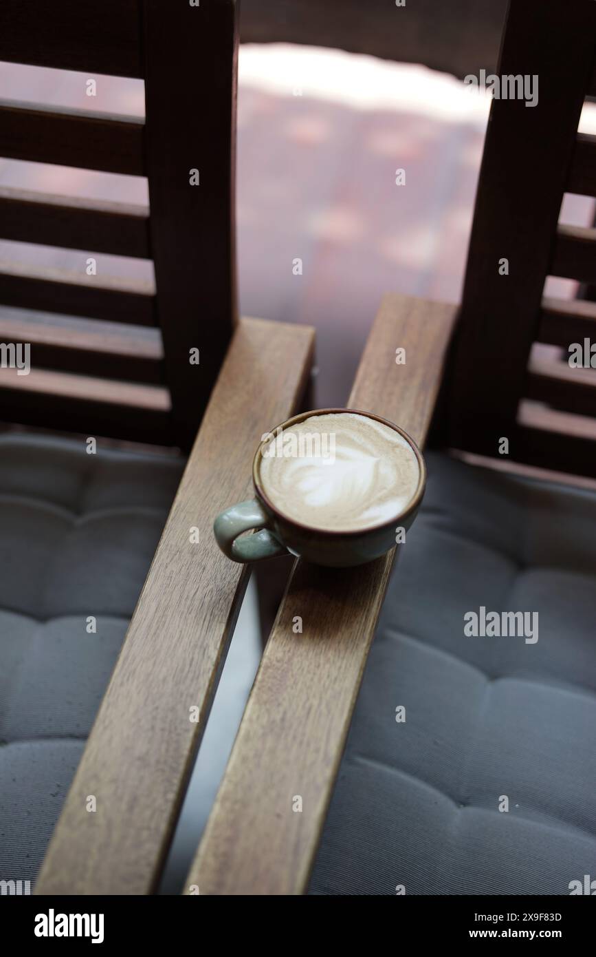 Heißer Kaffee Latte Vintage Tasse auf traditionellem Holzsessel am Fenster ästhetische Sofortaufnahme. Stockfoto
