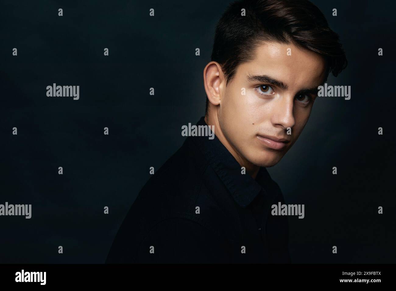 Porträt eines hübschen jungen Mannes in Schwarz vor schwarzem Hintergrund Stockfoto