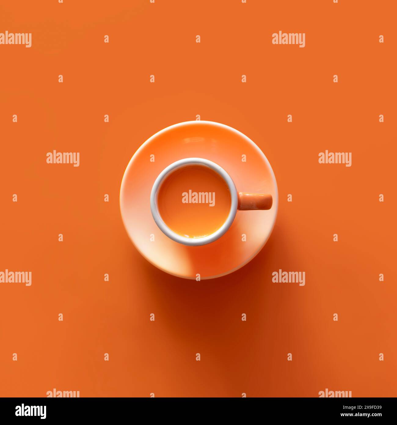 Blick von oben auf eine orangene Tasse gefüllt mit einem Heißgetränk auf einem orangen Hintergrund Stockfoto