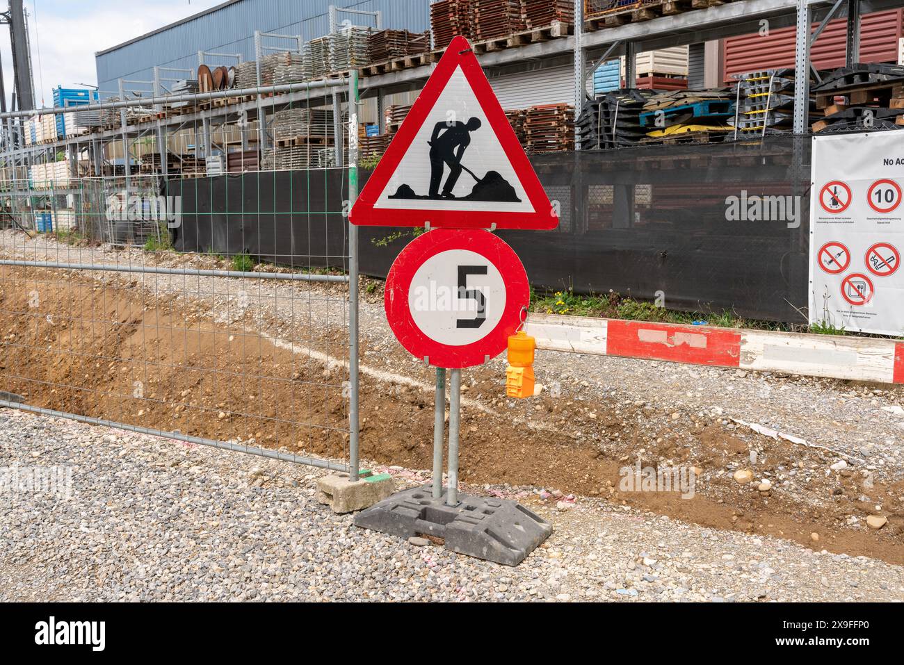 Baustelle mit Schotterstraße, einem Geschwindigkeitsbegrenzungsschild mit 5 km/h und einem Schild zur Baustelle, neben anderen Warnschildern. Stockfoto