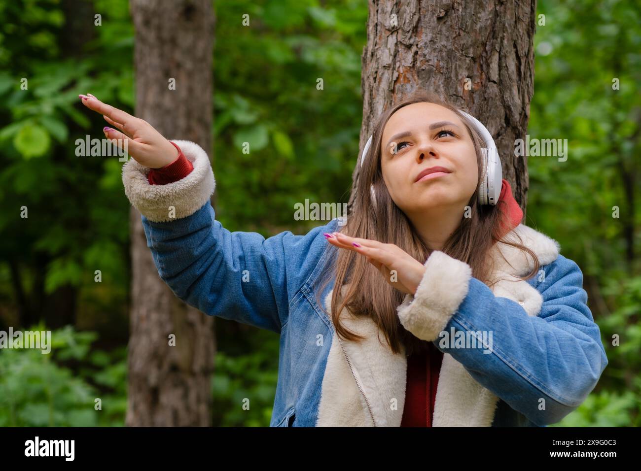 Eine junge Frau lehnt sich an einen Baum, trägt Kopfhörer und genießt Musik im Wald an einem sonnigen Nachmittag Stockfoto