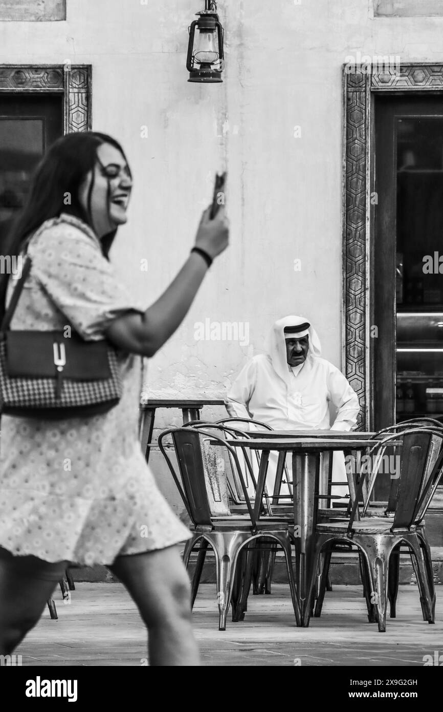 Doha, Katar - 1. Mai 2024: Ein traditioneller katarischer Mann im Souq Waqif in Doha und ein Mädchen, das im Vordergrund vorbeizieht, ohne den Fokus auf Absicht zu richten Stockfoto