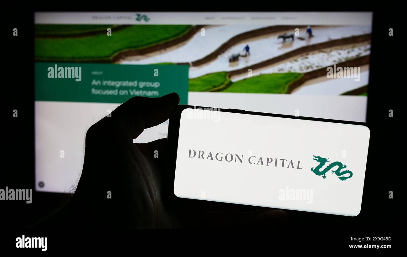 Person mit Smartphone und Logo der vietnamesischen Firma Dragon Capital Group Limited vor der Website. Schwerpunkt auf dem Display des Telefons. Stockfoto