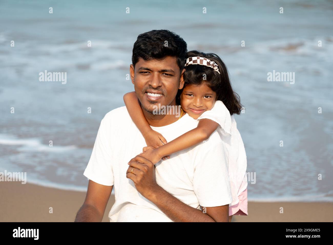 Ein ruhiger Strandtag, den ein Vater und seine kleine Tochter teilen. Ihre liebevolle Umarmung fängt einen kostbaren Familienmoment ein. Stockfoto